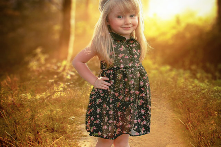 Girl in black and pink floral sleeveless dress stands in a pathway