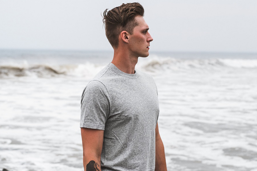 Homem posando com uma camisa de manga curta perto do mar