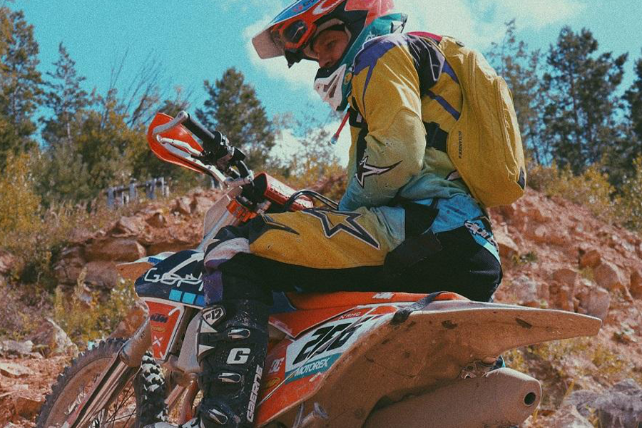 Homem de terno amarelo de moto posando com uma bicicleta laranja