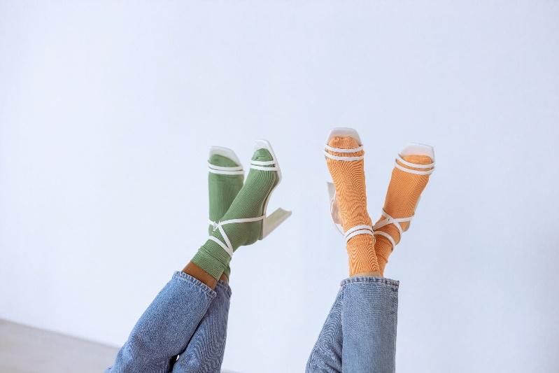 Frauen tragen grüne und orangefarbene Socken und weiße Riemchensandaletten