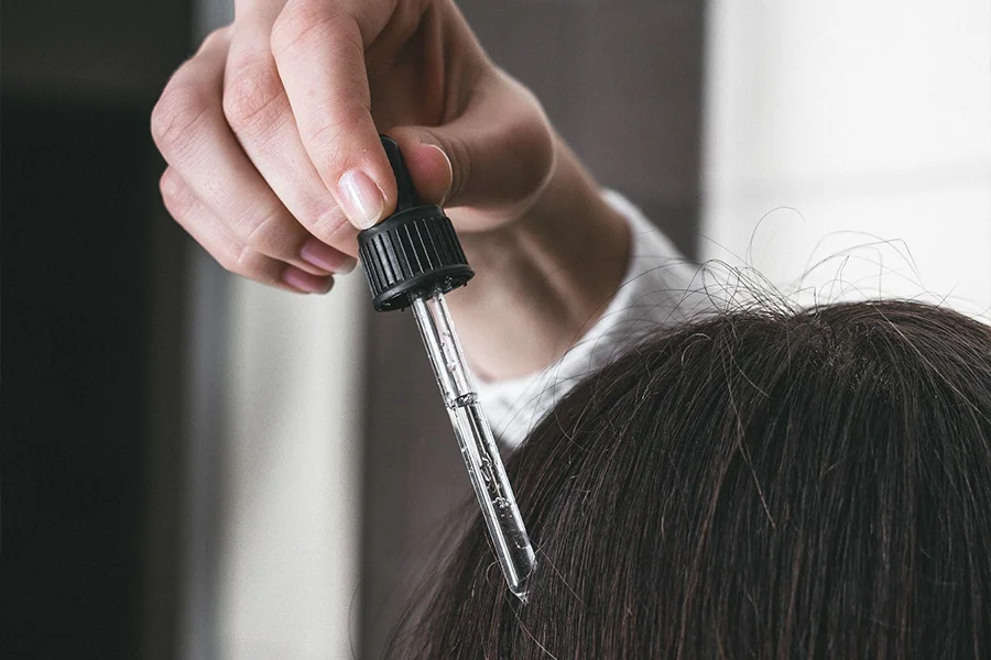 Mujer con cabello oscuro aplicando suero para el cuero cabelludo