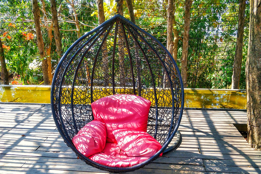 una silla de huevo colgante en un patio con almohadas rosas