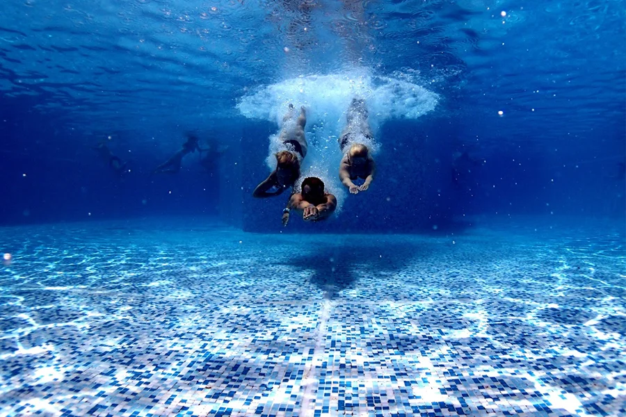 Hombres zambulléndose en la piscina con mosaicos azules y blancos