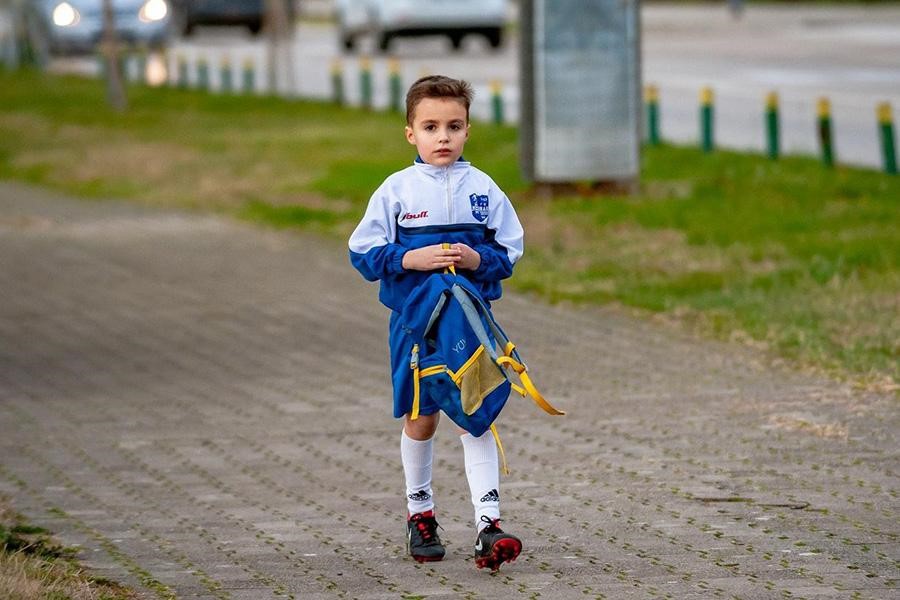 Anak laki-laki berjaket putih dan biru berjalan di jalan bata