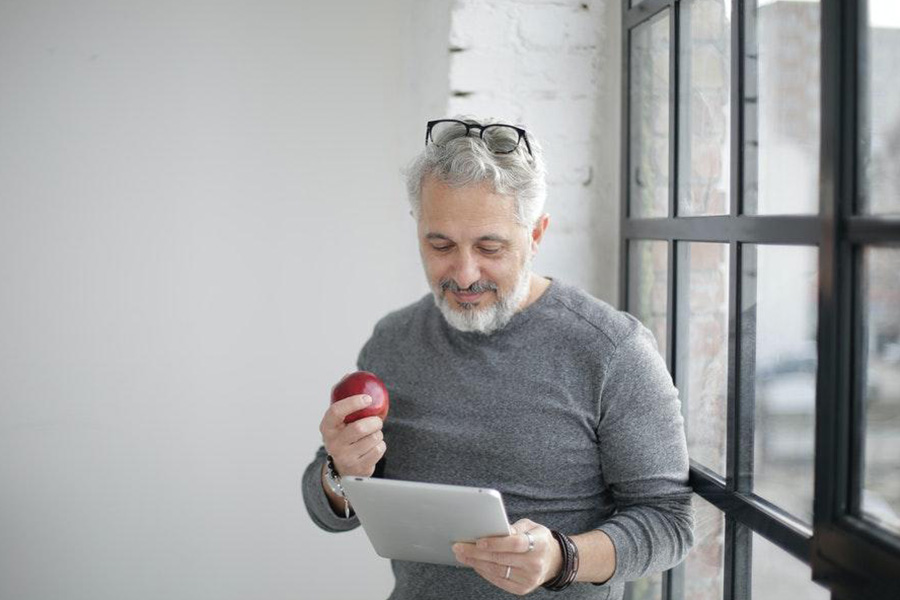 Homme âgé berçant un t-shirt gris à manches longues et tenant une pomme