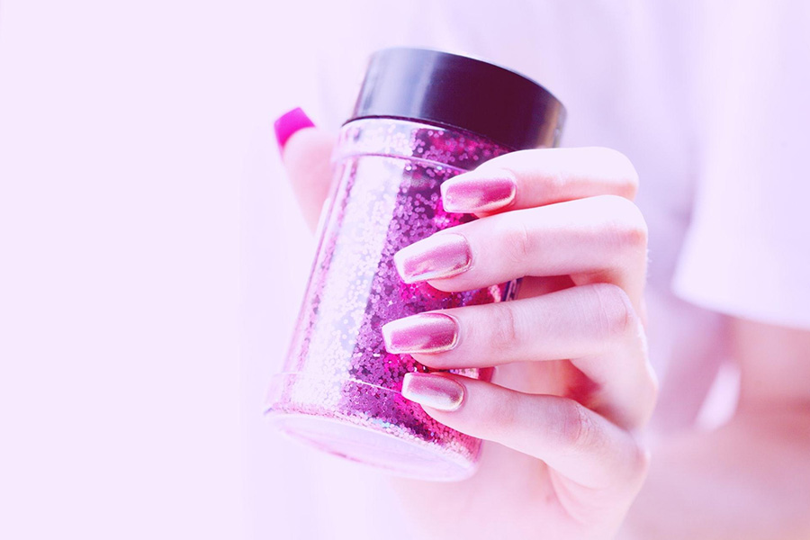 Une femme tenant un vernis à ongles pailleté rose