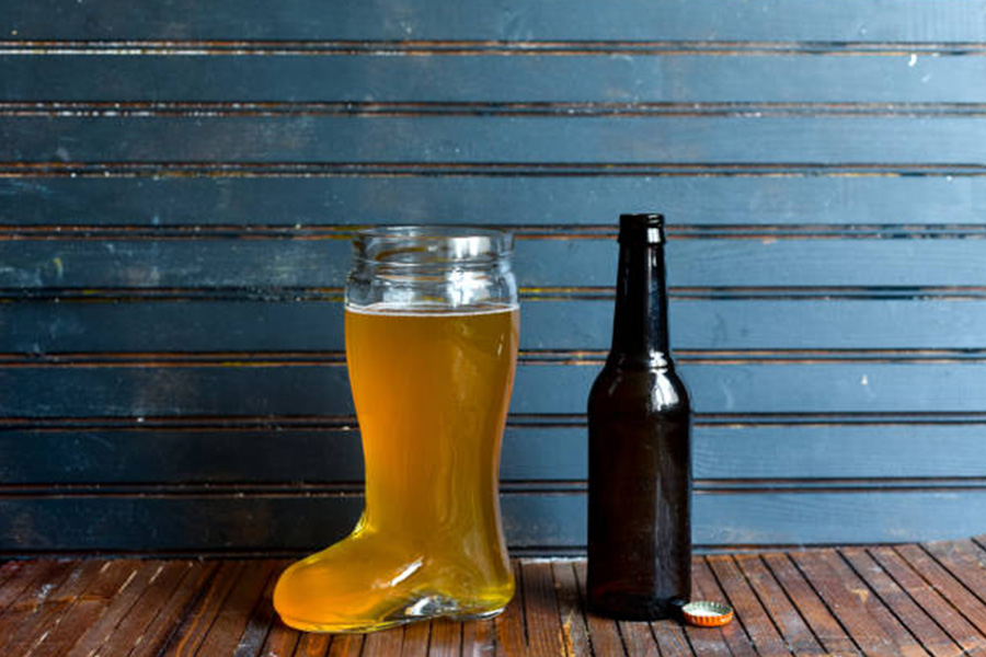 Vaso de cerveza en forma de bota junto a una botella