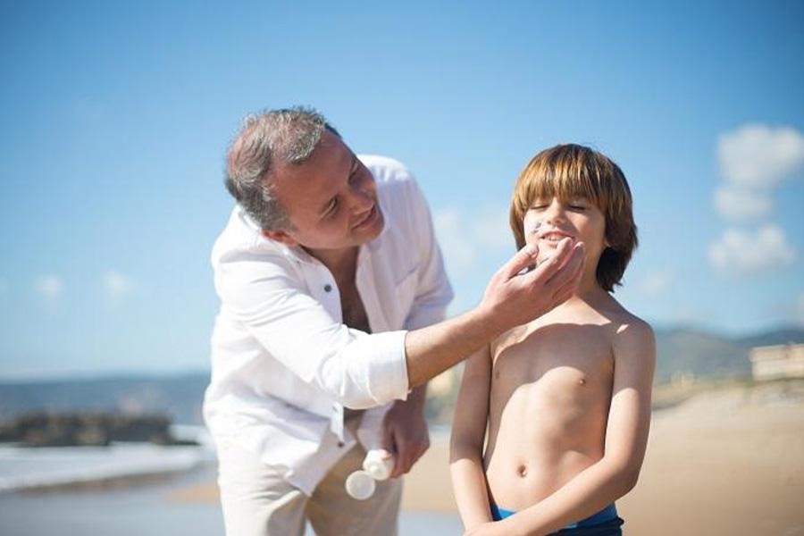 Uomo che applica una crema solare per la cura della pelle sul viso di un ragazzo in una giornata di sole