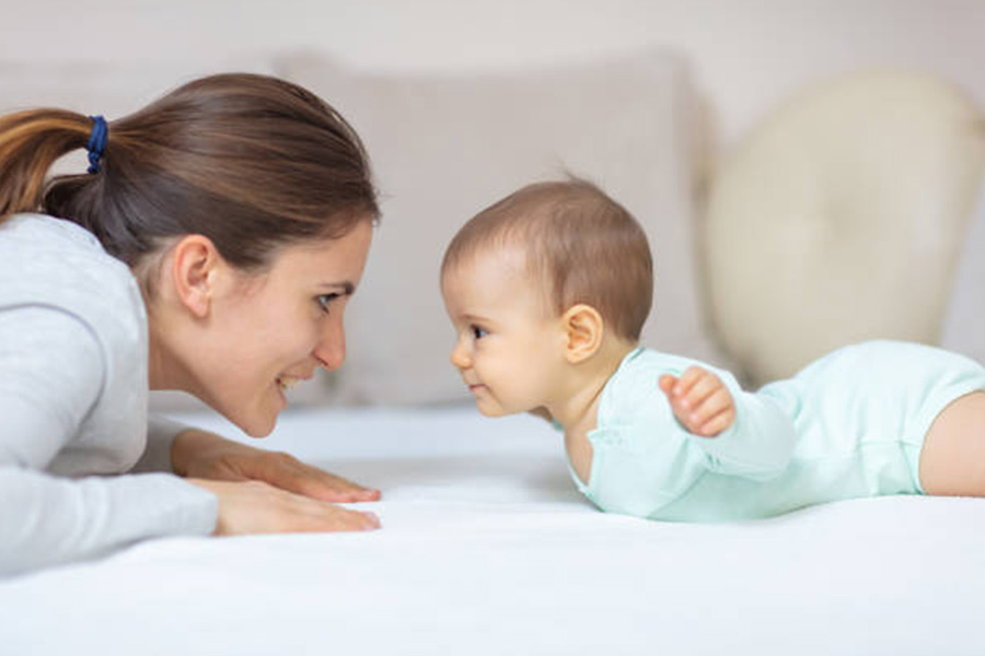 Mutter mit Kind im hellblauen Babystrampler im Bett