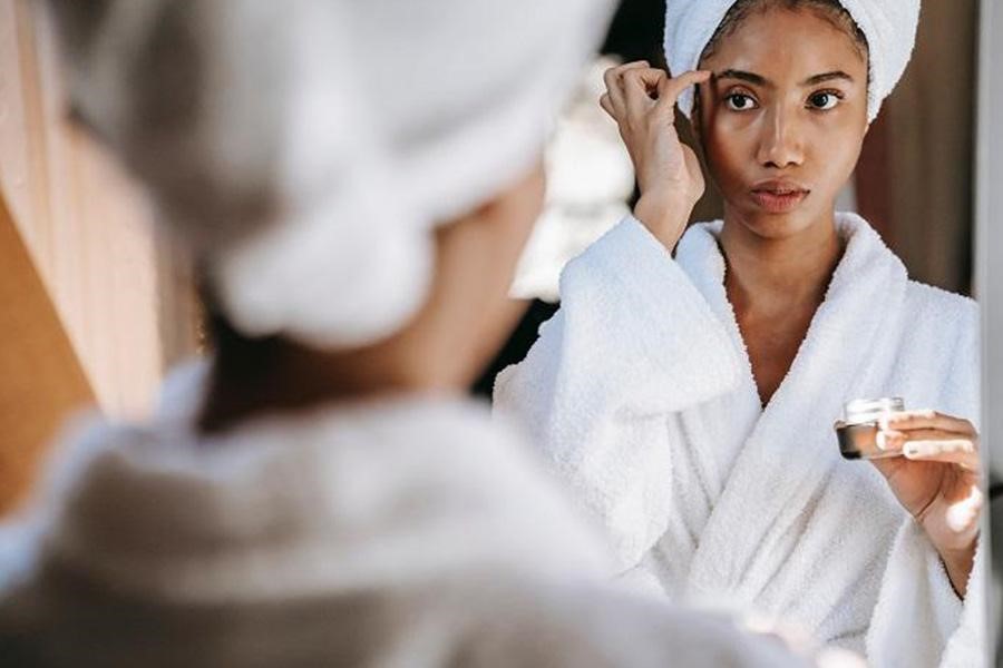 Femme en peignoir appliquant une crème hydratante pour les yeux sur son visage