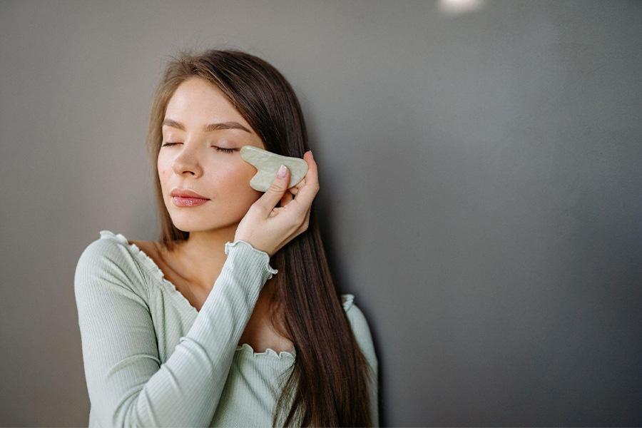 Mulher massageando o rosto com um gua sha