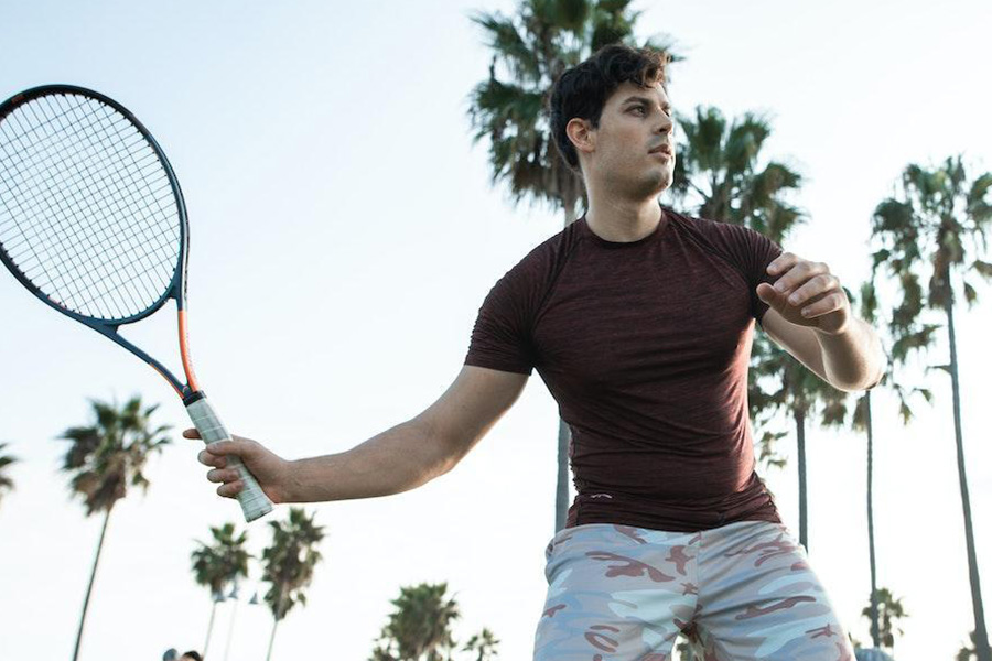 Mann posiert mit braunem Tech-T-Shirt und Tennisschläger