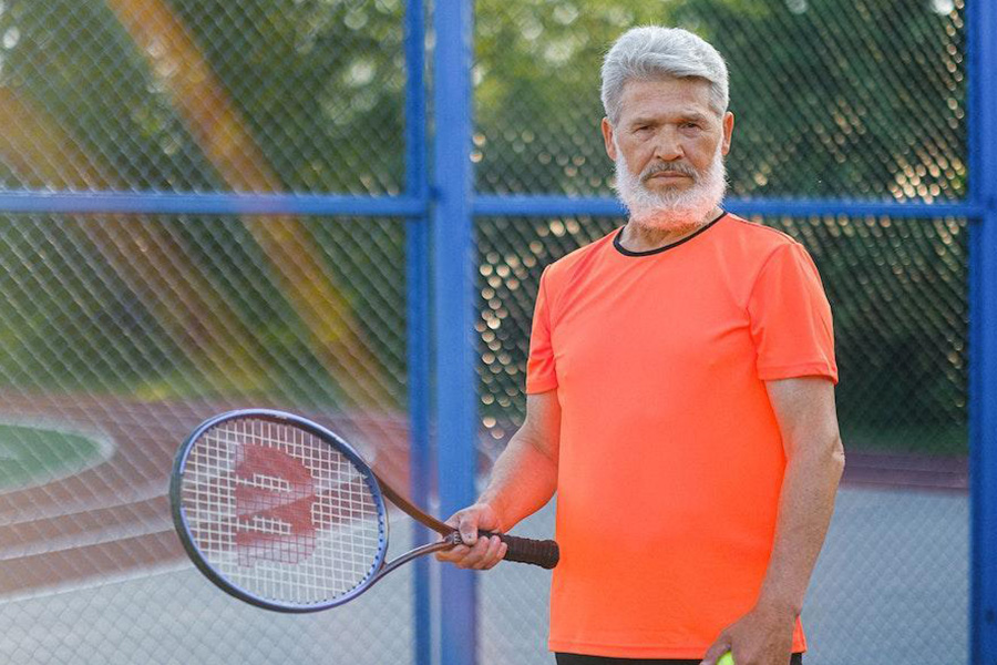 Mann trägt ein orangefarbenes Tech-T-Shirt mit Tennisschläger