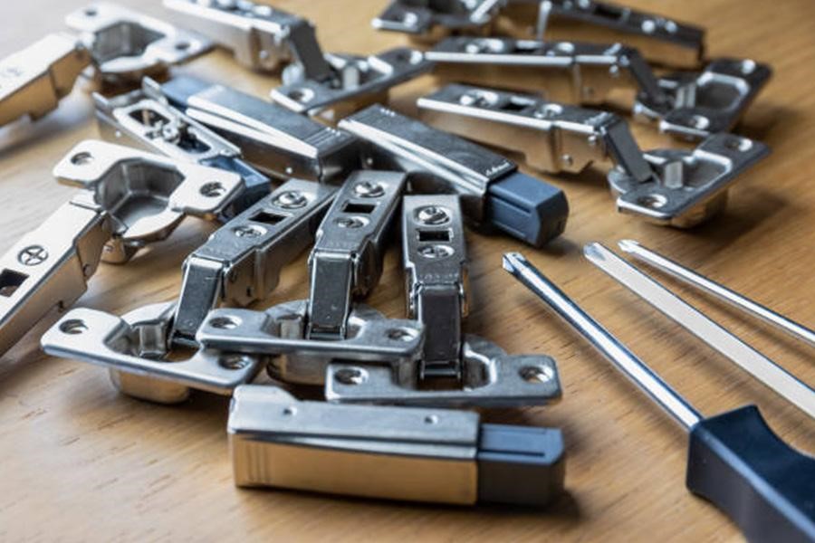 Various furniture hinges on a table with screwdrivers