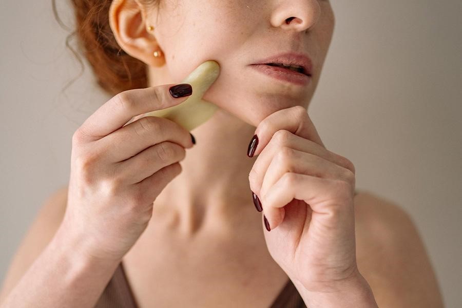 Femme exécutant la technique de soin de la peau Gua Sha avec un outil en pierre