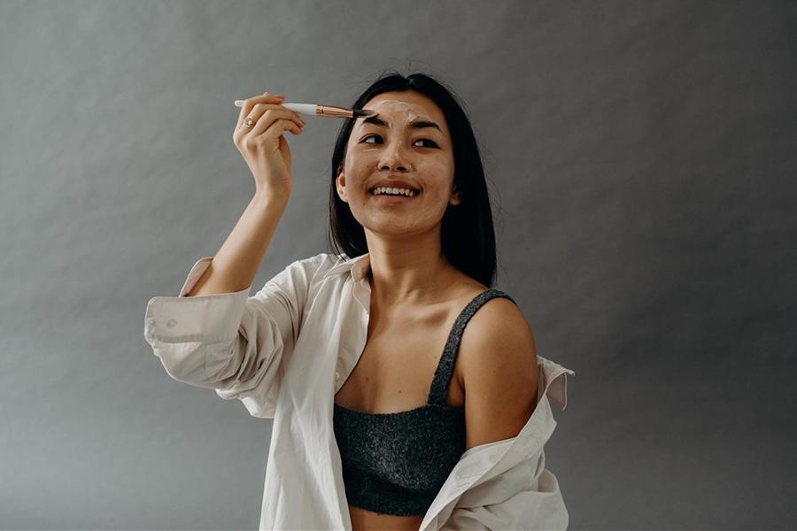 Young woman using facial brush to apply skincare product