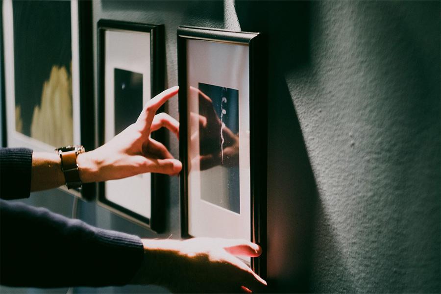 A person adjusting picture frames on wall