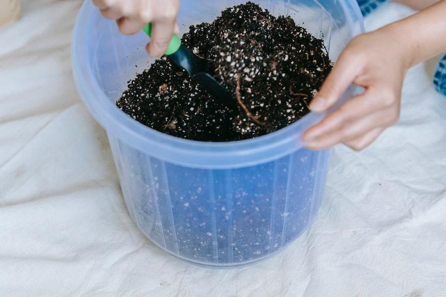 Personne anonyme plaçant de la terre dans un pot en plastique