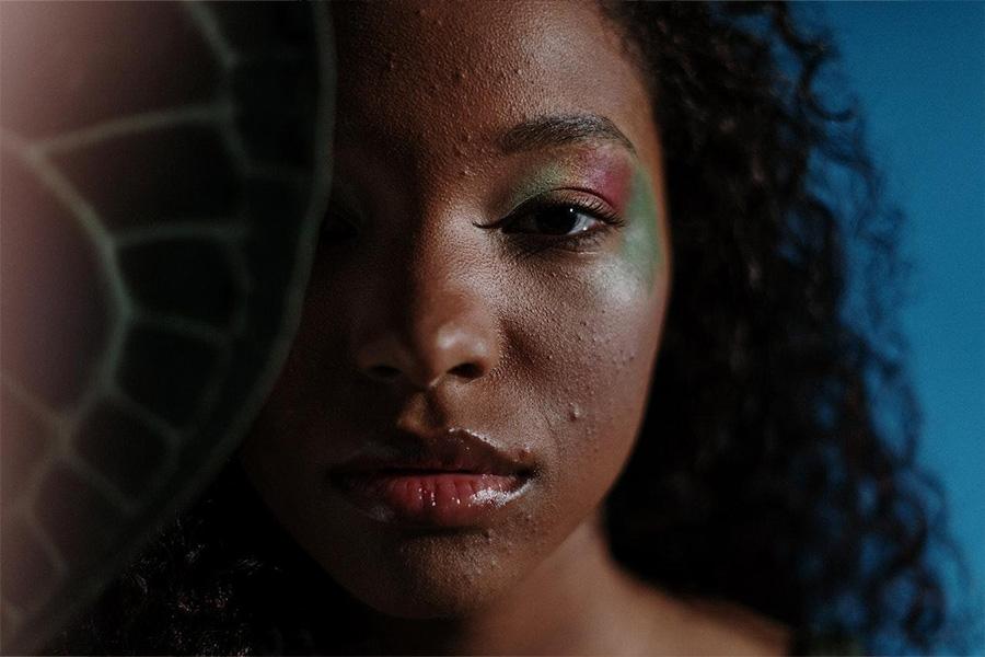 Femme noire portant un maquillage rose et vert avec une peau imparfaite