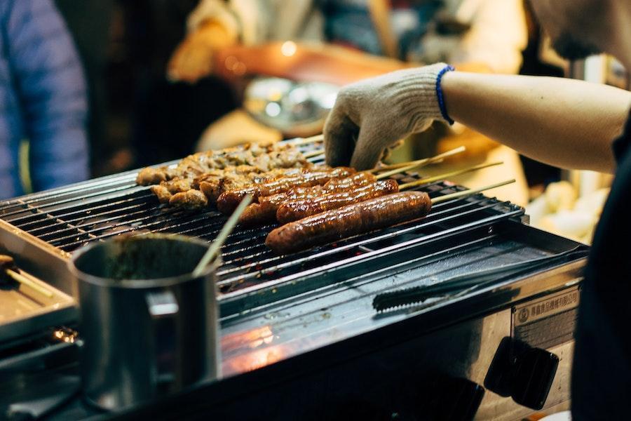 Hombre asando salchichas en una parrilla de gas