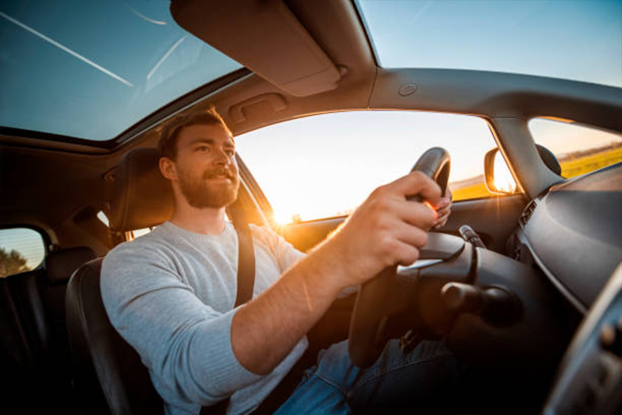 Uomo che sembra felice di guidare la sua macchina al tramonto