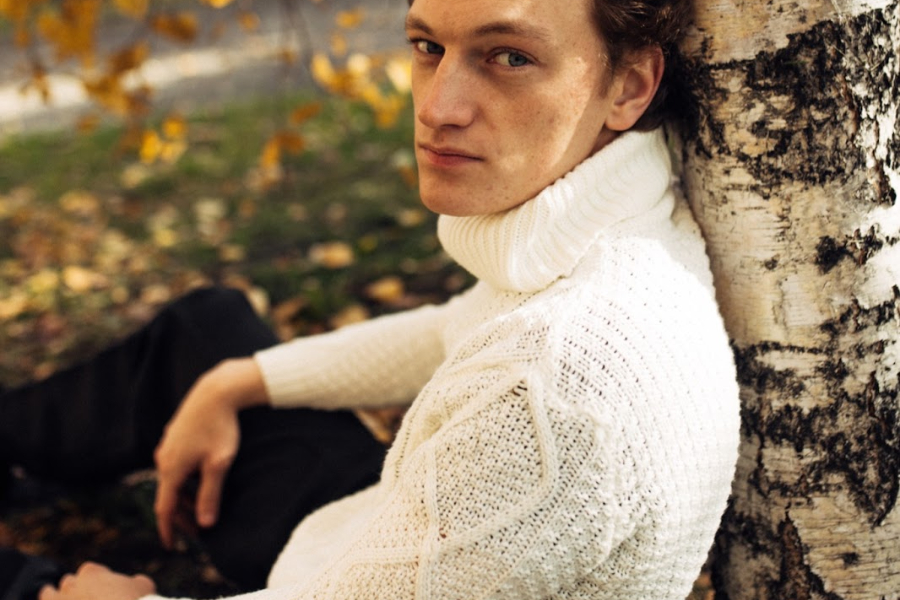 Man wearing a cream open-weave sweater by a tree