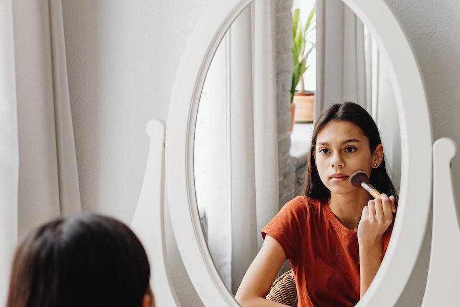 Tween trägt Make-up vor einem Spiegel auf