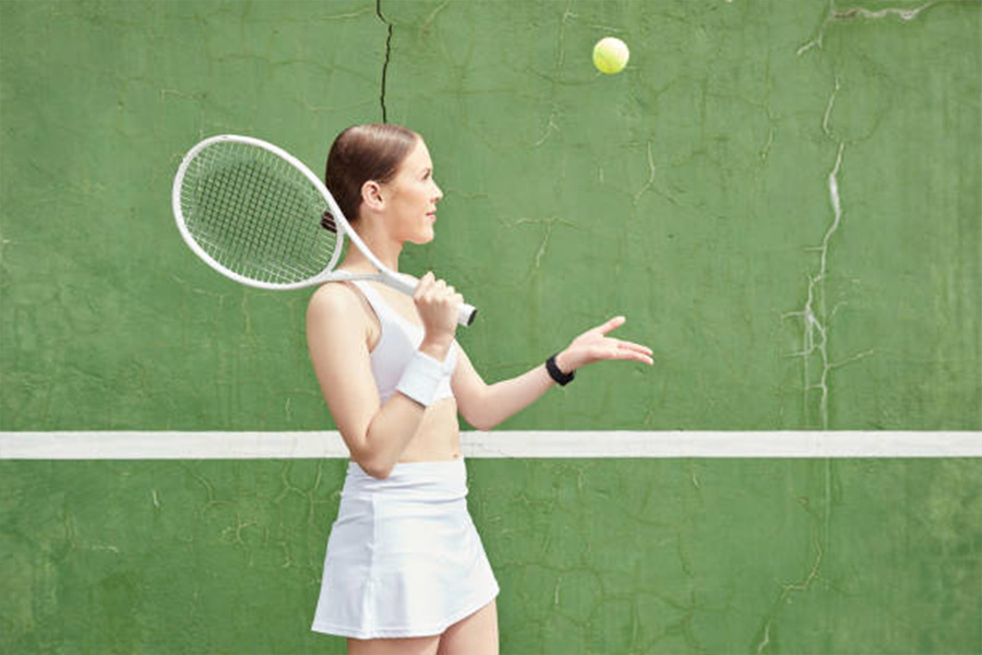 Mulher com roupa de tênis branca jogando bola no ar