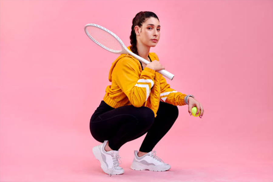 Wanita dengan jaket oranye antik memegang raket tenis dan bola