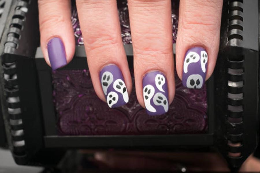 Unhas de mulher pintadas de roxo com fantasmas brancos no topo