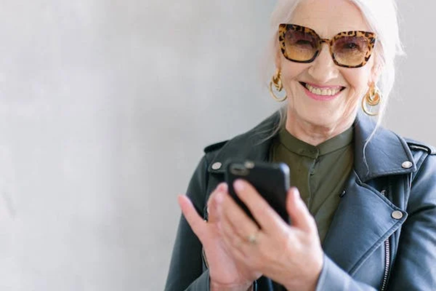 Allegra donna in menopausa che usa lo smartphone con gli occhiali alla moda