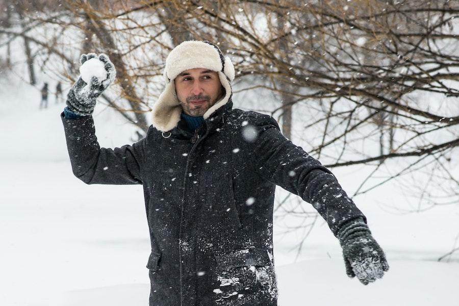 Mann hält einen Schneeball und schaukelt dabei einen Trapperhut