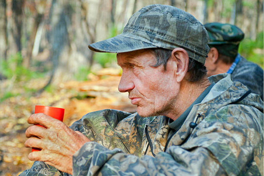 Man sitting in forest wearing camouflage clothes and cap