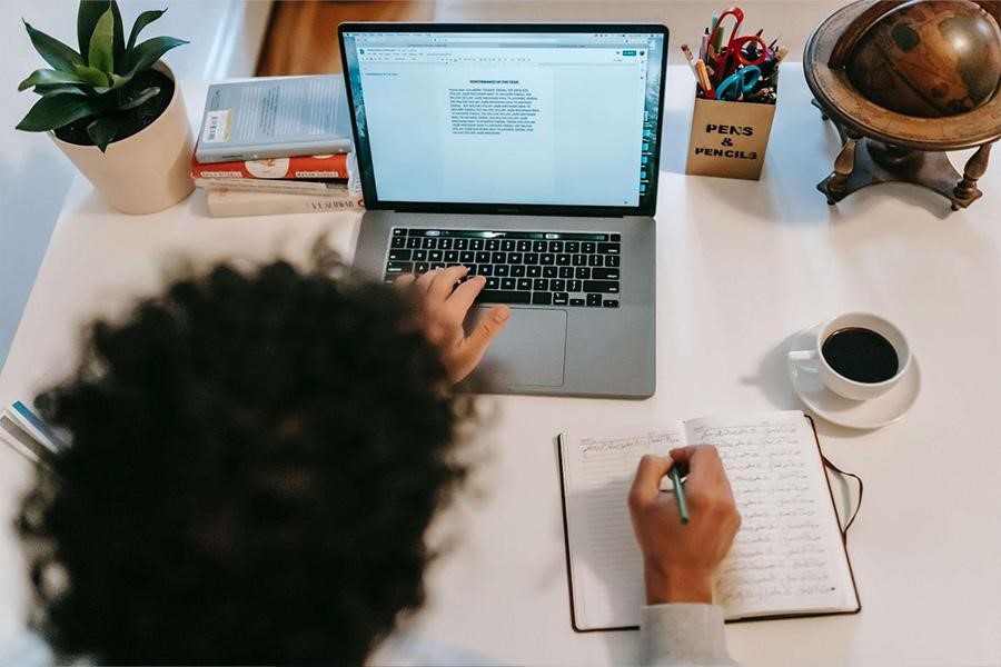 Person writing on a notepad, and working an open laptop