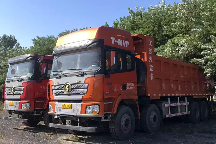 Two Shaanxi trucks parked in an open field