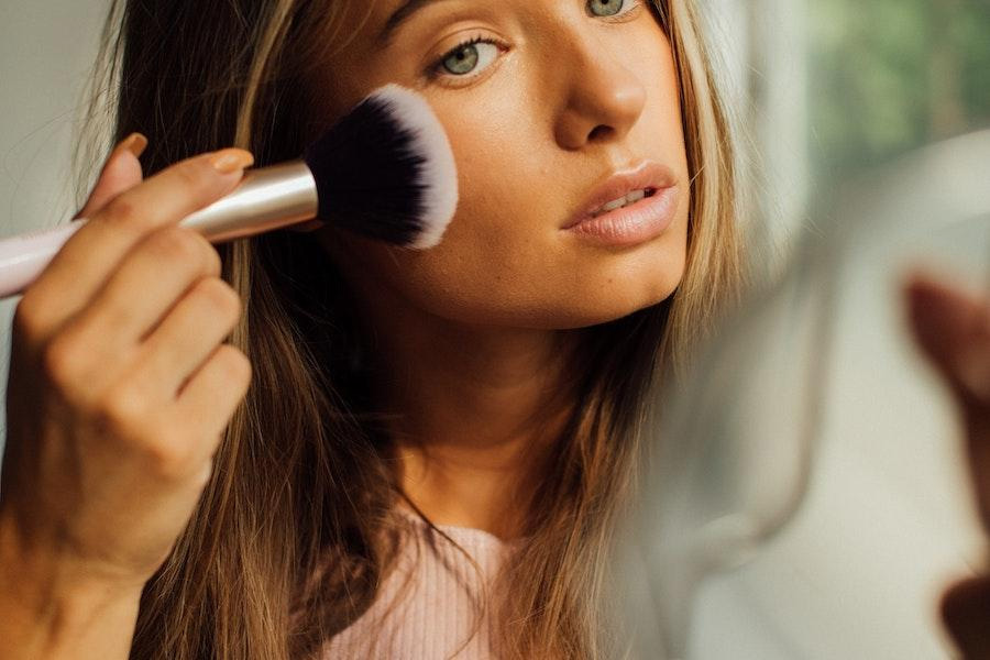 Mujer sosteniendo un pincel de maquillaje mientras aplica cosméticos