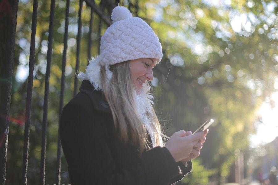 Donna che tiene il telefono mentre indossa un berretto con pompon