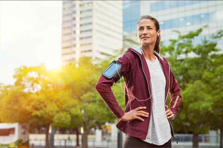 Frau macht mit Activewear-Jacke und Kopfhörern eine Laufpause