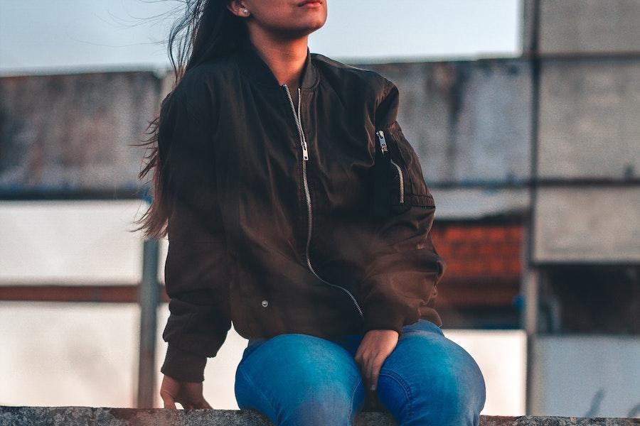 Femme assise sur une clôture avec un blouson noir