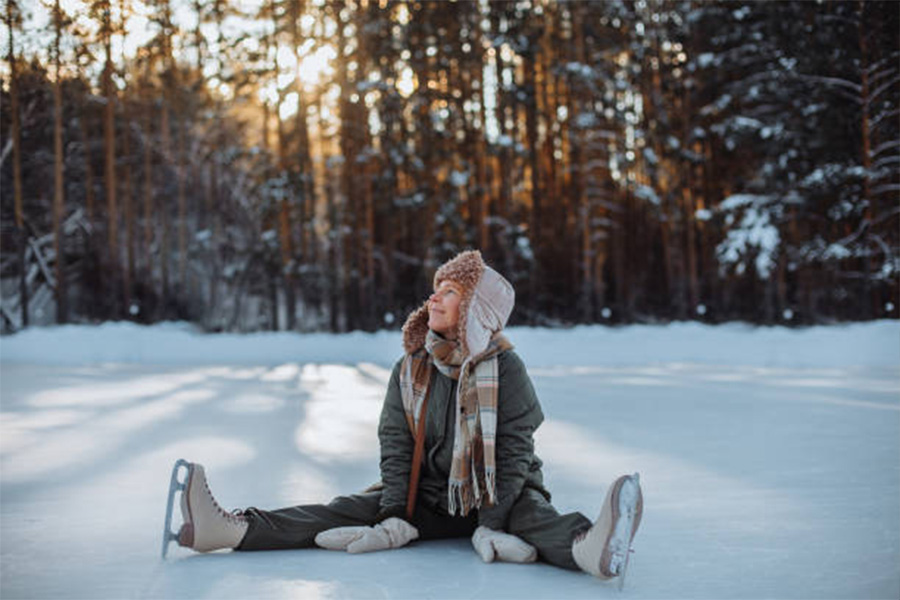 Femme assise sur la glace en patins avec chapeau de trappeur