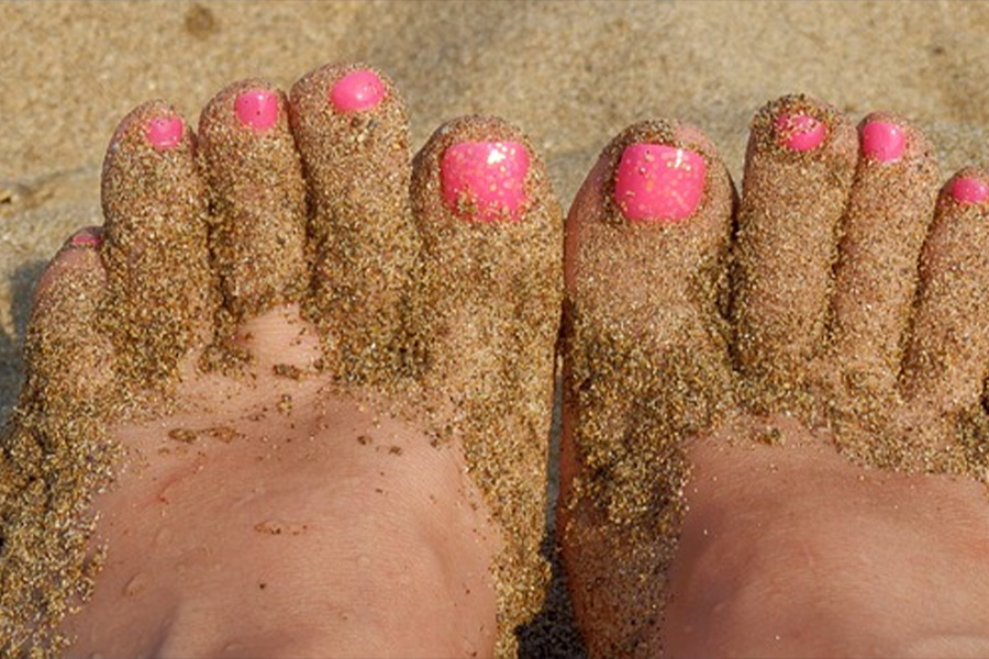 Pés de areia de mulher com esmalte rosa choque.