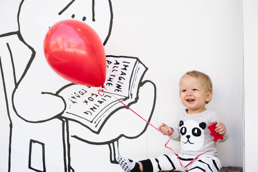 Un bébé tenant un ballon rouge dans une barboteuse pour bébé