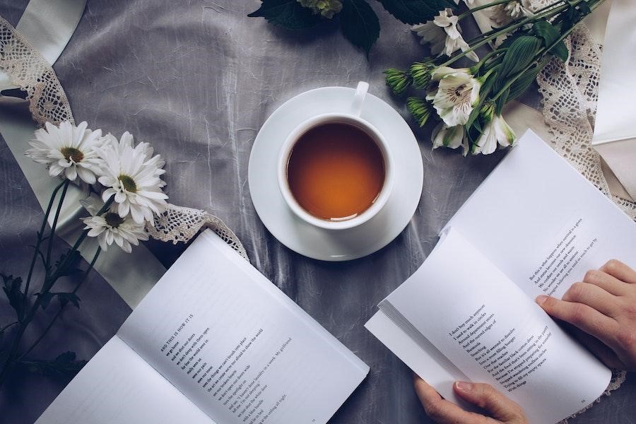 Persona anónima leyendo un libro cerca de una taza de café.