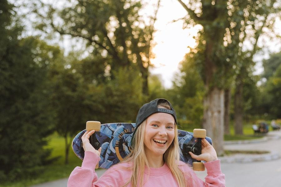 Senhora loira vestindo um boné de beisebol e segurando um skate