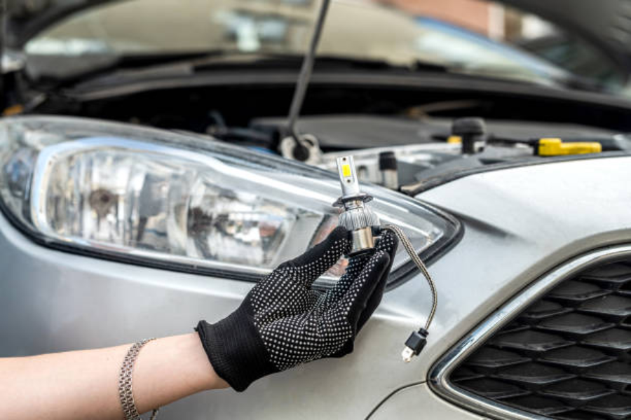 Uma mão segurando uma lâmpada LED moderna perto de um farol de carro