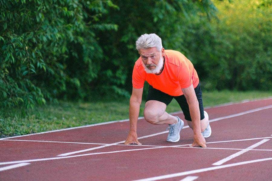 Hombre en posición de carrera con camiseta naranja y pantalones cortos