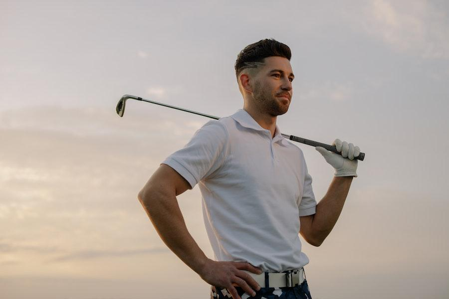 Homem posando com taco de golfe enquanto usa polo branco