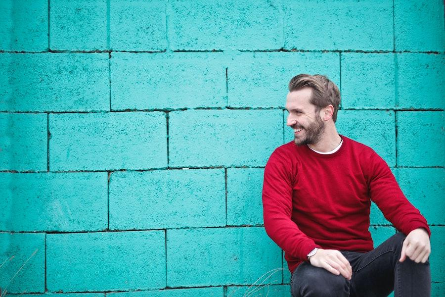 Man smiling sideways in a red sweatshirt and jeans outfit