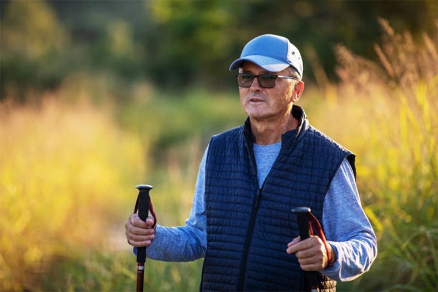 Uomo con bastoncini da trekking che indossa un berretto da baseball e occhiali da sole