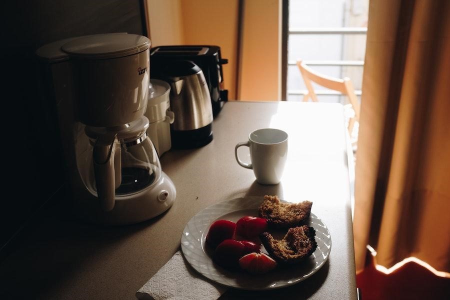 Cafetera de servicio individual cerca de una taza y desayuno